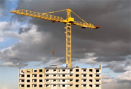 simsearch:400-06075932,k - Hoisting crane lifting a concrete slab on a house being built, on the background of gloomy thunder clouds Fotografie stock - Microstock e Abbonamento, Codice: 400-05052006