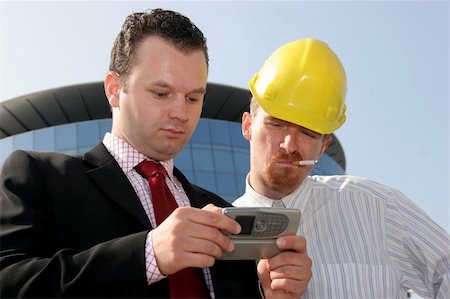 simsearch:400-04180586,k - Young businessman showing something on a cell phone(PDA), to a construction worker in front of a corporate building Stockbilder - Microstock & Abonnement, Bildnummer: 400-05074870