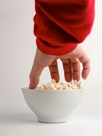 A hand trying to reach some popcorns from a bowl. Stock Photo - Budget Royalty-Free & Subscription, Code: 400-05078862