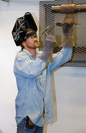 simsearch:400-04032937,k - Welder hammering a piece of metal he's been welding.  Focus on the man's face.  (helmet was customized by the welder - the designs are not trademarked or copyrighted) Photographie de stock - Aubaine LD & Abonnement, Code: 400-05081272