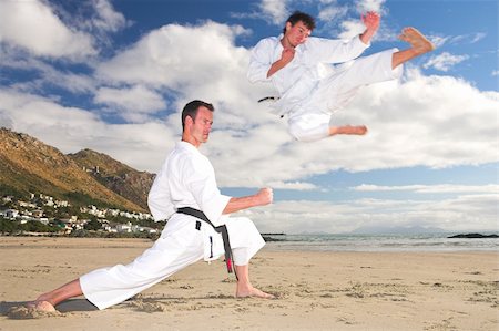 play fight - Young adult men with black belt practicing on the beach on a sunny day. The man doing the flying kick in the background has movement. Focus on the standing man Foto de stock - Super Valor sin royalties y Suscripción, Código: 400-05083174