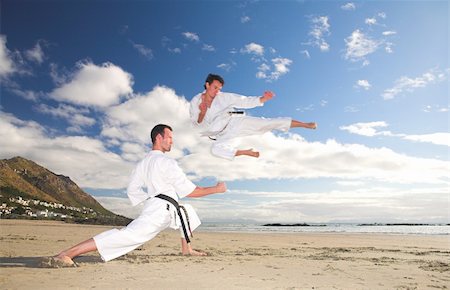 play fight - Young adult men with black belt practicing on the beach on a sunny day. The man doing the flying kick in the background has movement. Focus on the standing man Foto de stock - Super Valor sin royalties y Suscripción, Código: 400-05083173