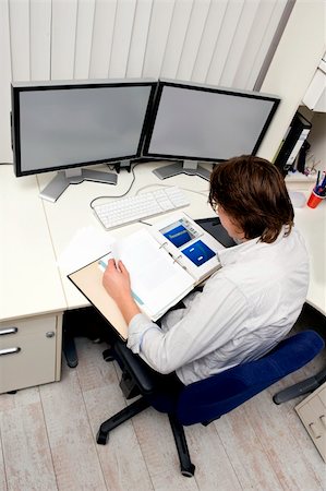 an engineer studying a thick dossier behind his desk with two computer screens on it Stock Photo - Budget Royalty-Free & Subscription, Code: 400-05095444