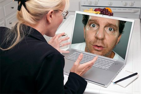 Shocked Woman In Kitchen Using Laptop with Strange Man on Screen. Screen can be easily used for your own message or picture. Picture on screen is my copyright as well. Foto de stock - Super Valor sin royalties y Suscripción, Código: 400-05106627