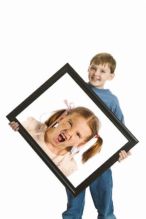 rivalidade entre irmãos - Grinning boy holding a portrait of his sister looking dirty and furious. Isolated on a white background. Foto de stock - Royalty-Free Super Valor e Assinatura, Número: 400-05109122