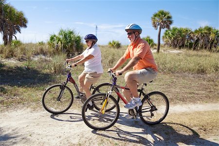 seniors bike riding on beach - Senior couple riding bikes at the beach, wearing sunglasses and helmets.  Focus on the woman. Stock Photo - Budget Royalty-Free & Subscription, Code: 400-05116405