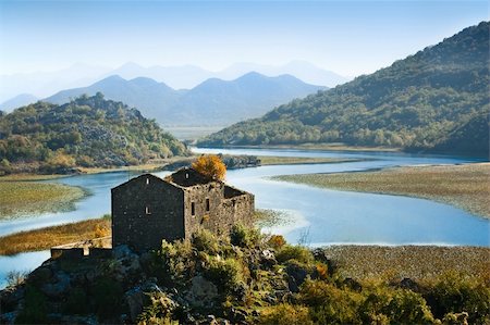 siege - Ruined medieval castle and still river in Montenegro. Hills covered with woods and blue misty mountain range on the background Stock Photo - Budget Royalty-Free & Subscription, Code: 400-05117108