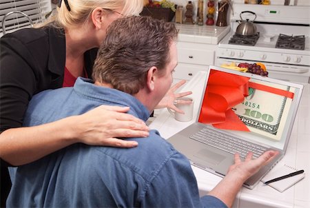 Couple In Kitchen Using Laptop with Stack of Money Wrapped in a Red Ribbon on the Screen. Stock Photo - Budget Royalty-Free & Subscription, Code: 400-05129323