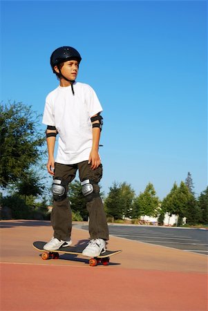 Teenage boy riding a skateboard on the sidewalk of a parking lot on a sunny day with blue sky and trees in the background. Stock Photo - Budget Royalty-Free & Subscription, Code: 400-05120048