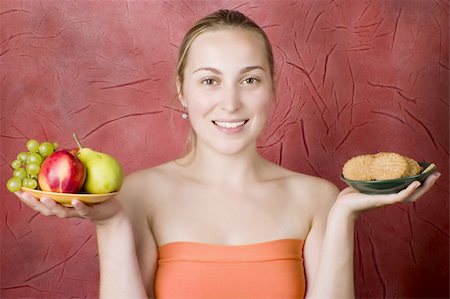 photo of model woman with grapes - Smiling young woman on a diet. Girl choosing food: fruits or cookies. Red background. Stock Photo - Budget Royalty-Free & Subscription, Code: 400-05147334