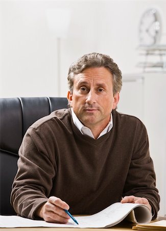 Attractive male sitting at desk with pen and paper, looking at camera. Vertical Stock Photo - Budget Royalty-Free & Subscription, Code: 400-05154315