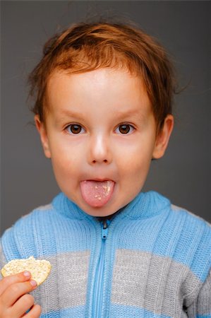 Portrait of a little boy in a blue sweater with a cookie showing his tongue Stock Photo - Budget Royalty-Free & Subscription, Code: 400-05155467