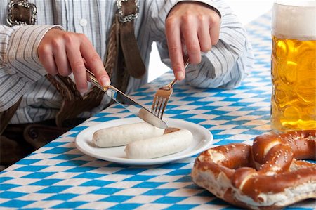 simsearch:400-04680527,k - Bavarian man dressed in traditional leather trousers (lederhosen) is eating a veil sausage (Weisswurst) and beside him is a full beer stein (Maß) and pretzel. Stockbilder - Microstock & Abonnement, Bildnummer: 400-05161876