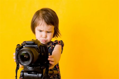 Portrait of baby girl holding photo camera isolated on yellow background Fotografie stock - Microstock e Abbonamento, Codice: 400-05174346