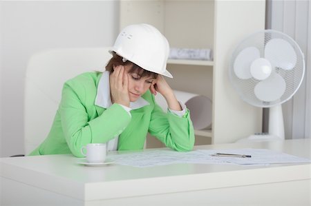 Sad woman the engineer with a helmet on a head sits at a table on a workplace Stock Photo - Budget Royalty-Free & Subscription, Code: 400-05178567