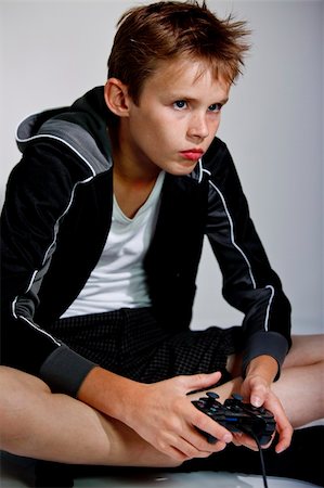 Boy contrating on playing a computer game, sitting on the floor with a controller or joystick  in his hands Stock Photo - Budget Royalty-Free & Subscription, Code: 400-05186061