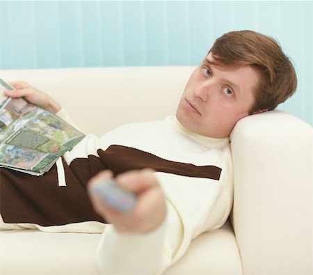 simsearch:400-05195435,k - A young man, lying on the couch with a magazine and the TV remote control Stockbilder - Microstock & Abonnement, Bildnummer: 400-05195437