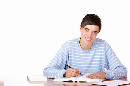 simsearch:400-04704759,k - Young student is sitting on desk with open book and learns for his exams. He looks smiling into camera. Isolated on white. Stock Photo - Budget Royalty-Free & Subscription, Code: 400-05196623