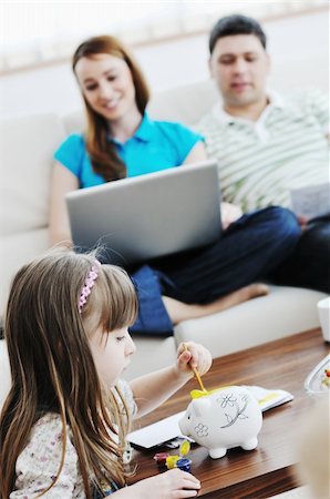 young happy family at bright and modern living room puting money in piggy bank and working on laptop computer on home finance Stock Photo - Budget Royalty-Free & Subscription, Code: 400-05211268