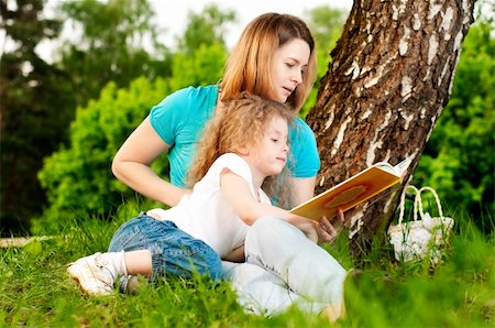 simsearch:400-05248187,k - young mother sitting in grass under tree and reading book to her small daughter who is lying on knees of her mother and smiling Photographie de stock - Aubaine LD & Abonnement, Code: 400-05234382