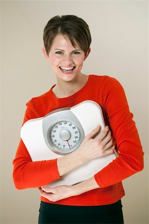 edbockstock (artist) - Attractive young woman holds a bathroom scale to her chest while smiling at the camera. Vertical shot. Photographie de stock - Aubaine LD & Abonnement, Code: 400-05239909