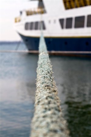 A view of a big boat in the background, ready to sail, focused on the sharp details of the rope, using shallow depth of field Need for escape, need for holidays Foto de stock - Super Valor sin royalties y Suscripción, Código: 400-05253419