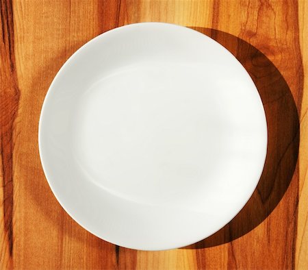 Pure white porcelain dinner plate on kitchen hard wood table with shadow. Fotografie stock - Microstock e Abbonamento, Codice: 400-05284330