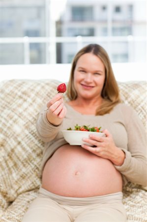 simsearch:400-04266869,k - Future mother showing a strawberry to the camera sitting on the sofa Stock Photo - Budget Royalty-Free & Subscription, Code: 400-05285287