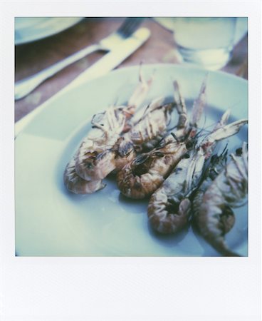 six unpeeled king prawns on white plate, silverware and glassware in the background; blurred and moved Polaroid SX-70 Style, shot with original SX-70 Film with original paper frame Stock Photo - Budget Royalty-Free & Subscription, Code: 400-05292008