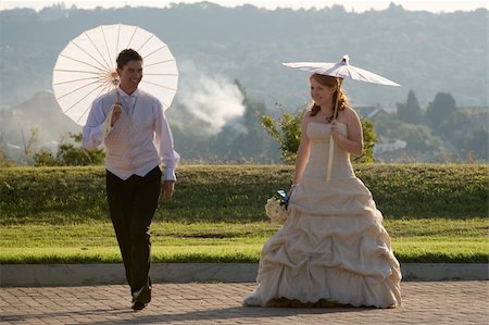 red head sexy beautiful bride and groom walking outside in sun with umbrellas jumping and smiling Stockbilder - Microstock & Abonnement, Bildnummer: 400-05302910