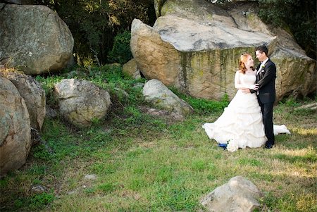 red head sexy beautiful bride in white and groom hugging and standing outside in sun next to boulders of rocks on green grass Stockbilder - Microstock & Abonnement, Bildnummer: 400-05302954