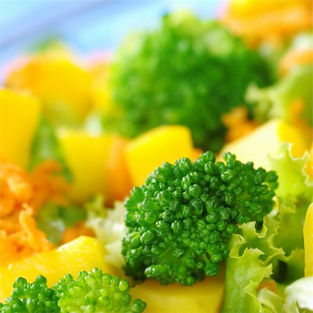 simsearch:400-04854606,k - Broccoli on fresh salad (broccoli, mango, carrot, lettuce) in a bowl with blue background (Very Shallow Depth of Field, Focus on the front of the broccoli) Foto de stock - Royalty-Free Super Valor e Assinatura, Número: 400-05320205