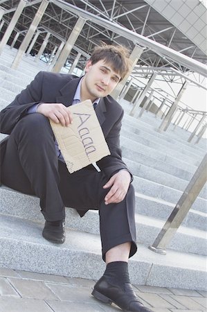 simsearch:400-08496169,k - Young businessman sitting on the stairs of the building in hand bumga cardboard with the text "aaaa.." with his other hand holding his head Stock Photo - Budget Royalty-Free & Subscription, Code: 400-05334376