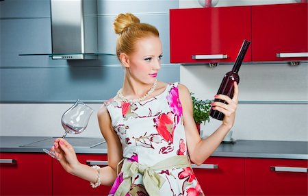 young beautiful blonde girl wearing white and pink dress holding glass and bottle of wine in interior of modern red kitchen in expectation of party Stockbilder - Microstock & Abonnement, Bildnummer: 400-05338536