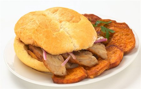 simsearch:400-04855335,k - Peruvian sandwich called Pan con Chicharron which is traditionally eaten for breakfast, and is prepared with fried pork and sweet potato and filled with ketchup and onions and served with fried sweet potato (Selective Focus, Focus on the front of the bun and the two meat slices on the right) Foto de stock - Royalty-Free Super Valor e Assinatura, Número: 400-05330785
