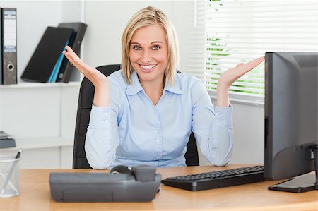 simsearch:400-04894274,k - Smiling blonde woman sitting behind desk not having a clue what to do next in an office Stock Photo - Budget Royalty-Free & Subscription, Code: 400-05345204