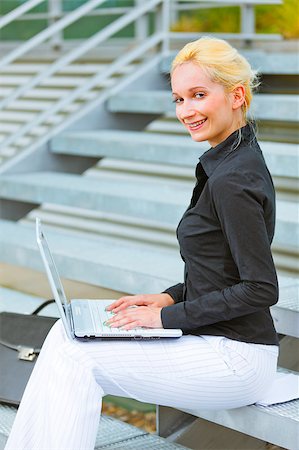 Smiling modern business woman sitting on stairs at office building and working on laptop Stock Photo - Budget Royalty-Free & Subscription, Code: 400-05341153