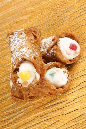 simsearch:400-05341443,k - Close-up of original mini sicilian cannoli on a transparent glass plate over a yellow background. These tube-shaped pastries are made of fried shells filled with a sweet mixture of ricotta cheese, chocolate, candied fruit and sprinkled with icing sugar. Stockbilder - Microstock & Abonnement, Bildnummer: 400-05342874