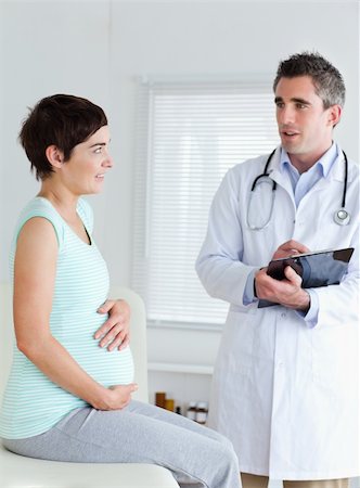 Sitting Pregnant woman touching her belly while talking to her doctor Stock Photo - Budget Royalty-Free & Subscription, Code: 400-05357205