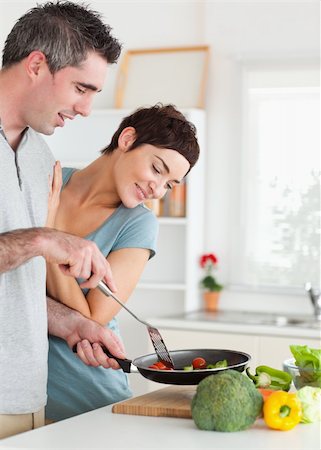 simsearch:400-05357733,k - Charming Woman looking into a pan her husband is holding in a kitchen Fotografie stock - Microstock e Abbonamento, Codice: 400-05357357