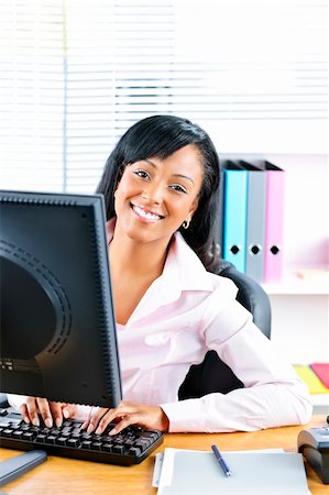 simsearch:400-04894274,k - Young smiling black business woman at desk typing on computer Stock Photo - Budget Royalty-Free & Subscription, Code: 400-05380305