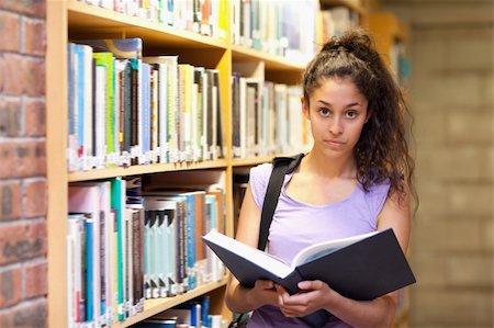 simsearch:400-05678140,k - Serious female student holding a book in a library Stockbilder - Microstock & Abonnement, Bildnummer: 400-05678137