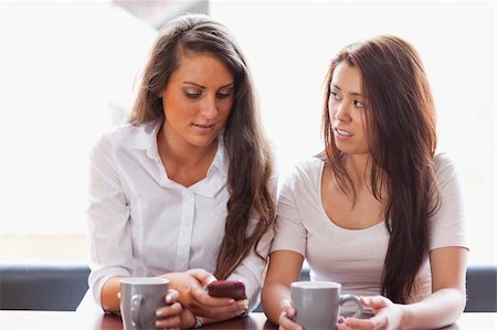 Beautiful friends looking at a smartphone while having a tea Stock Photo - Budget Royalty-Free & Subscription, Code: 400-05670055