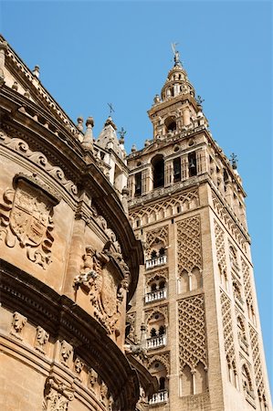 Detail of La Giralda Tower and Seville Cathedral. The bell tower (La Giralda) was previously a minaret of the Berber Almohad period in Spain. After the town was conquered by Christians, during the Reconquista period, the minaret was transformed and  in 1401 became the bell tower of the gothic and baroque Cathedral of Seville. Photographie de stock - Aubaine LD & Abonnement, Code: 400-05684389