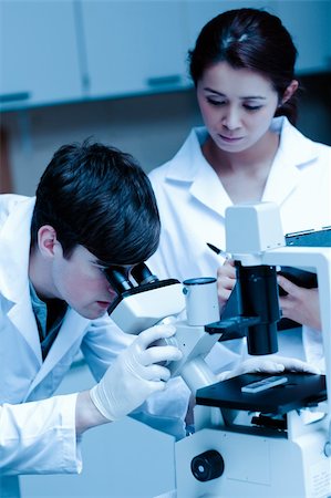 Portrait of a young scientist looking in a microscope while another is taking notes in a laboratory Stock Photo - Budget Royalty-Free & Subscription, Code: 400-05684505