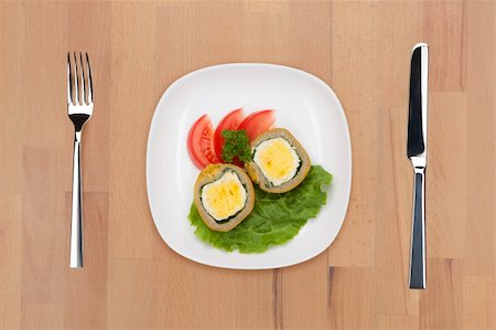 A plate with traditional Indian and Pakistani meal - nargizi kofta - on salad leafs with parsley and tomatoes with fork and knife on a wooden table. Stock Photo - Budget Royalty-Free & Subscription, Code: 400-05690794