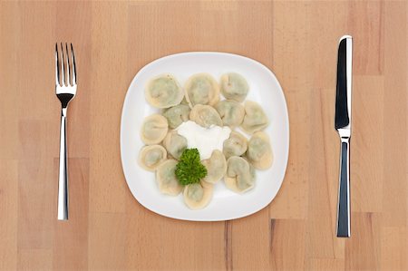 A plate with vegetarian ravioli decorated with parsley on a wooden table with fork and knife. Stock Photo - Budget Royalty-Free & Subscription, Code: 400-05690796