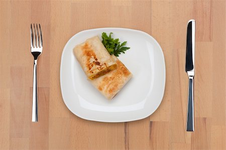 A plate with pieces of traditional Mexican burrito with forrk and knife on a wooden table. Stock Photo - Budget Royalty-Free & Subscription, Code: 400-05690801