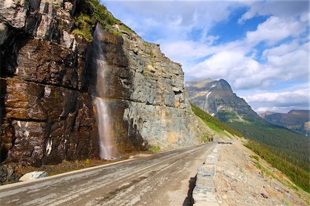 Waterfall flows down from the mountains onto the Going To The Sun Road in Glacier National Park - Montana. Foto de stock - Royalty-Free Super Valor e Assinatura, Número: 400-05705147