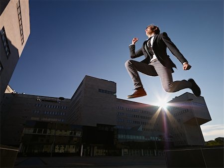 young business man jumping for joy outdoors, with office buildings and sun in background. Horizontal shape, side view, copy space Stock Photo - Budget Royalty-Free & Subscription, Code: 400-05705842